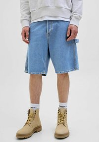 Lysblå denimshorts med en afslappet pasform og sidelommer. Kombineret med beige snørebodstøvler og hvide sokker.
