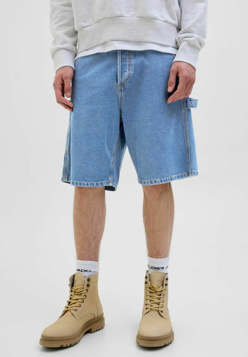 Lysblå denimshorts med en afslappet pasform og sidelommer. Kombineret med beige snørebodstøvler og hvide sokker.