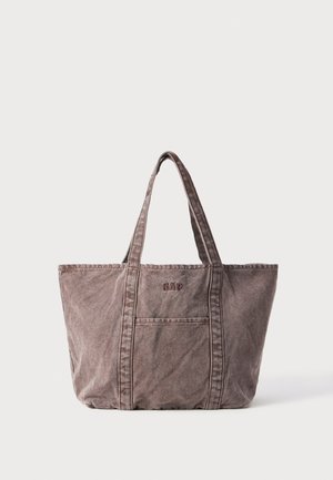 Ruskea kangaskassi, jossa on kaksi kestävää kahvaa. Edessä on tasku ja ommellut yksityiskohdat. Sanat "GAP" on esitetty tummalla tekstillä.