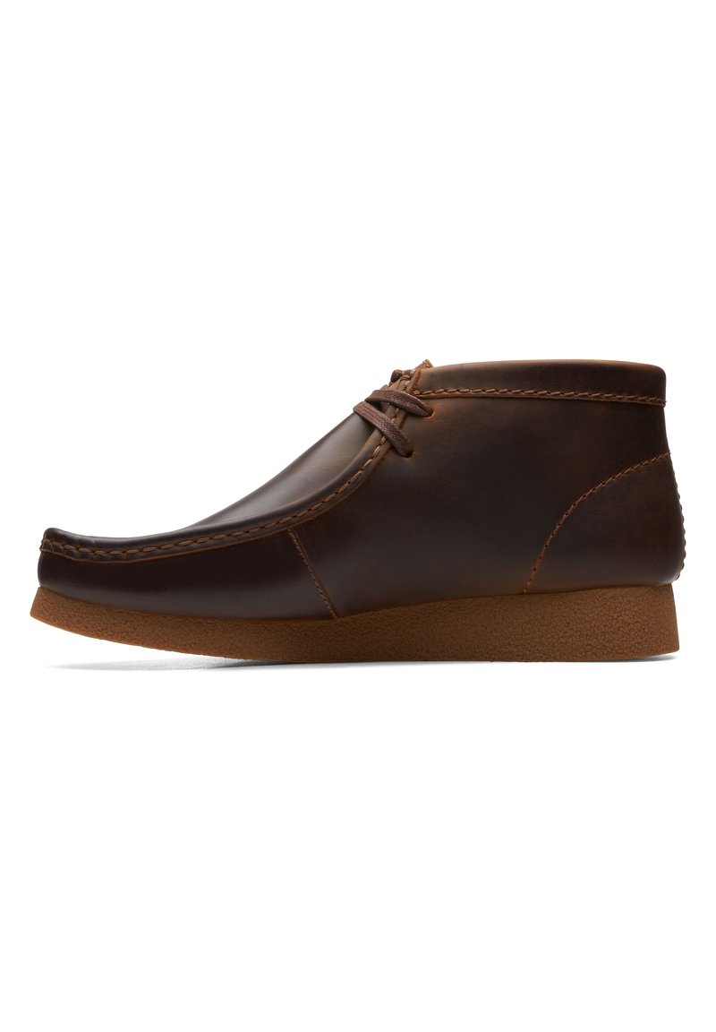 Botas de cuero marrón hasta el tobillo con punta redondeada, cordones mínimos y suela de goma en contraste. Presentan costuras visibles y un acabado suave.