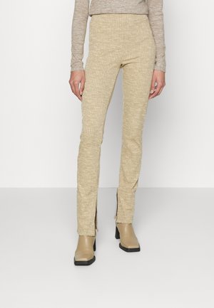 Calças de algodão beige com faixa elástica na cintura, apresentando aberturas laterais na bainha. Usadas com botins de salto bloco beige.
