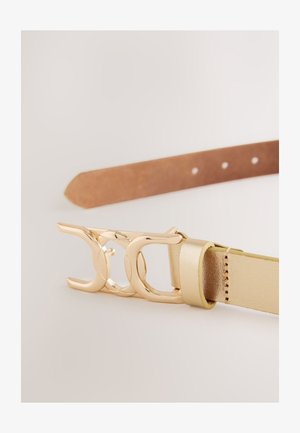 Auksinio atspalvio sagtis su susipynusiu dizainu pritvirtinta prie siauro, tekstūriniu smėlio spalvos odos dirželio. Penkios skylutės dydžio reguliavimui.