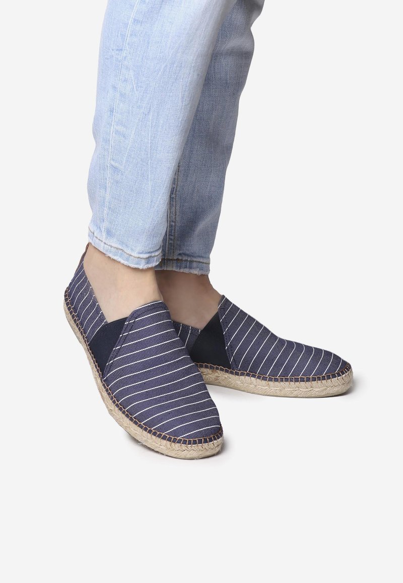 Jūrūno ir baltos dryžuotos espadrilės su kanapių viršumi, elastingomis šoninėmis panelėmis ir jutiška šlingelę. Dėvimos su šviesiai mėlynais pasuktais džinsais.