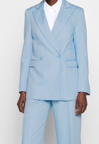 Blazer doppiopetto azzurro chiaro con revers a punta, due tasche anteriori e pantaloni coordinati, realizzato in tessuto liscio con una vestibilità sartoriale.