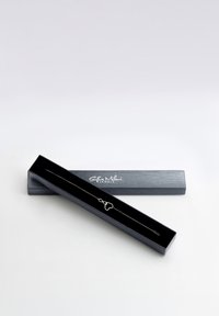 Silverhalsband med ett hjärtformat hänge, utställt i en öppen svart låda, med en slät yta och subtila logotyptryck på locket.