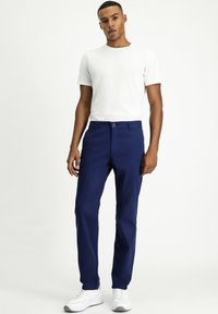 Pantalones azul marino con corte recto, hechos de algodón. Presentan un cierre de botón y bolsillos laterales, combinados con una camiseta blanca de cuello redondo.
