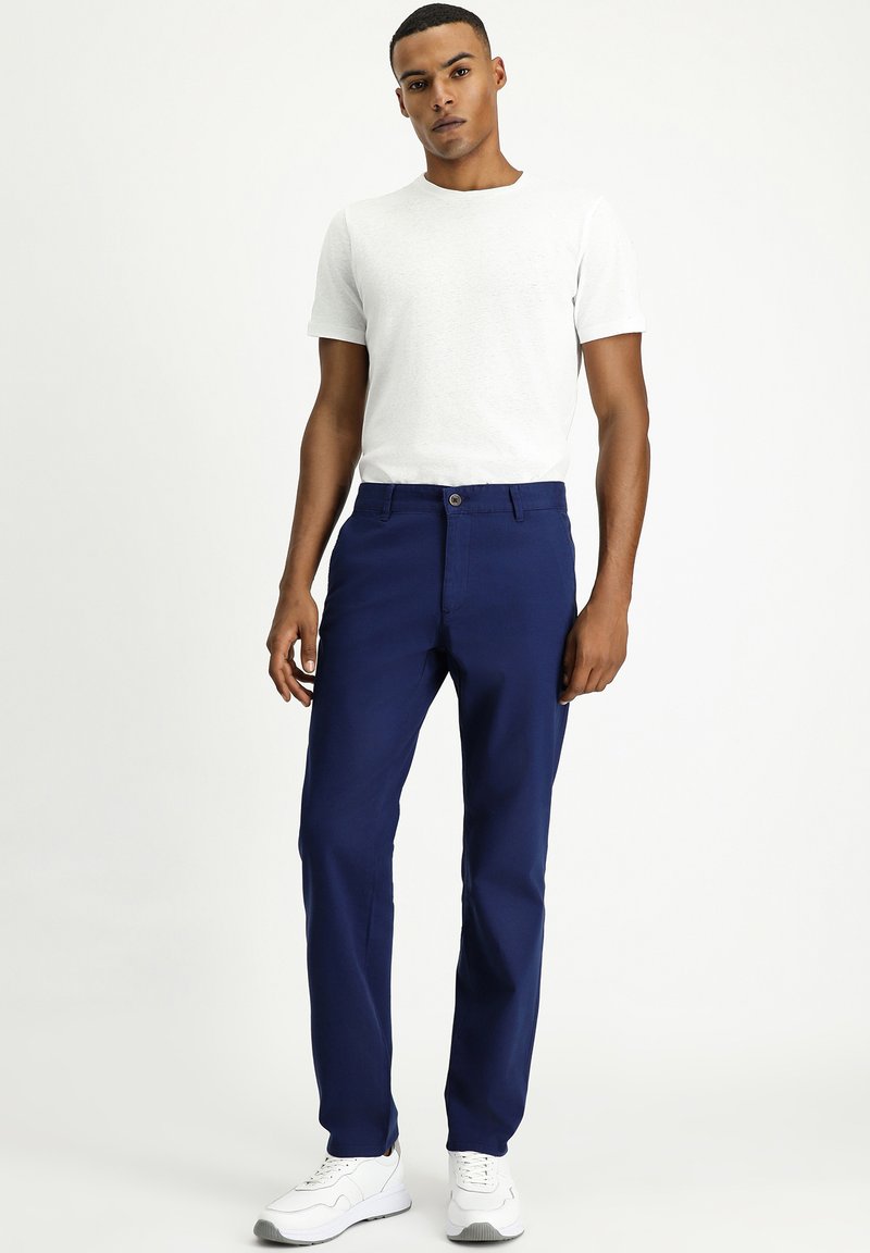 Pantalones azul marino con corte recto, hechos de algodón. Presentan un cierre de botón y bolsillos laterales, combinados con una camiseta blanca de cuello redondo.