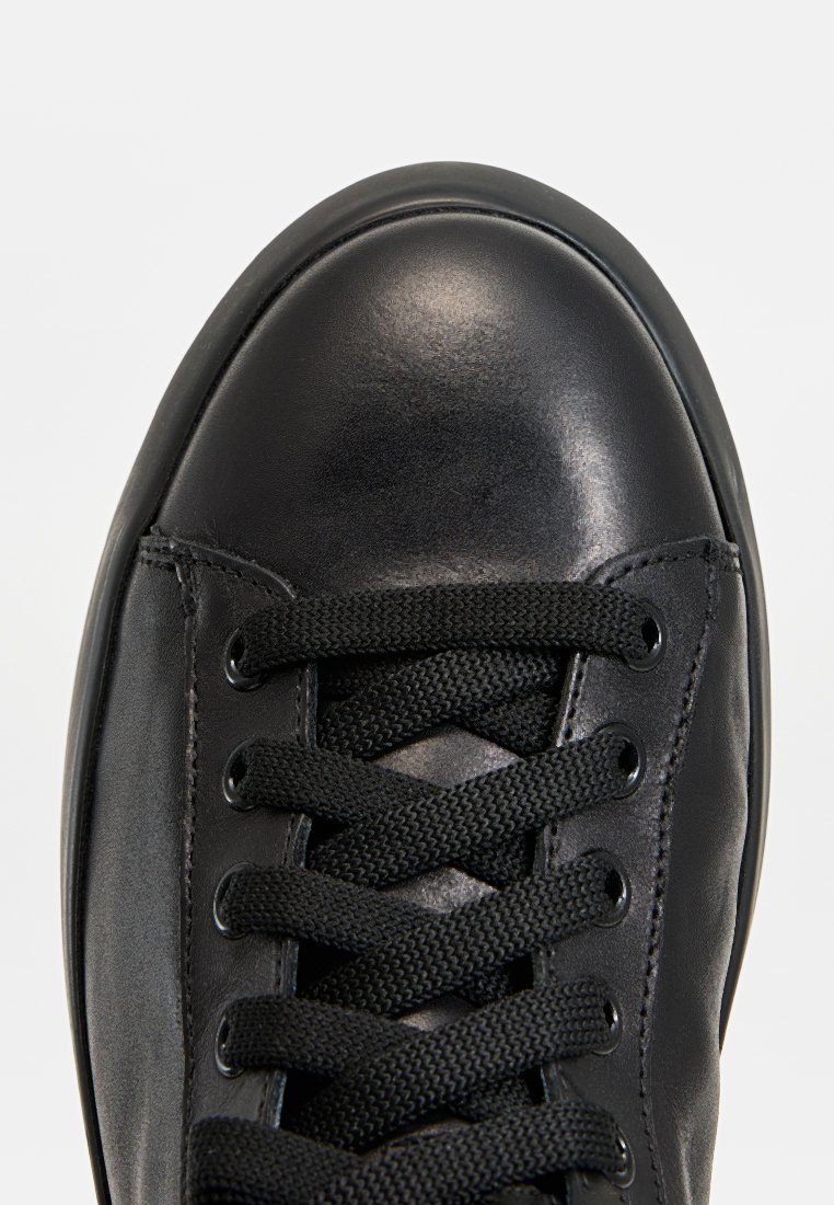 Schwarze Leder-Sneaker mit runder Zehenpartie, strukturiertem Obermaterial und schwarzen, geflochtenen Schnürsenkeln. Die Ösen für die Schnürsenkel sind an den Seiten sichtbar.