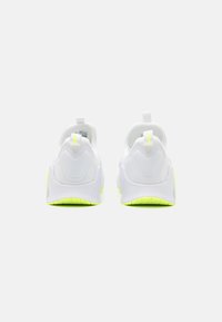 Hvide sports sneakers med en struktureret overdel, der har en livlig neon gul sål og bagakenter, designet til komfort og støtte.