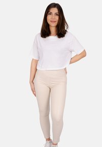 Weißes, kurzes T-Shirt, beigefarbene eng anliegende Leggings und weiße Sneaker. Glatte Texturen mit einem lässigen, entspannten Design.