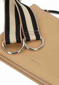 Hellbraune Ledertasche mit glatter Textur, ausgestattet mit zwei silbernen Ringen und einem schwarz-beige gestreiften Riemen. Markenname "Ted Baker" geprägt.