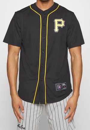 Mężczyzna ubrany w czarną koszulkę baseballową Pittsburgh Pirates z żółtymi przeszyciami oraz szare szorty w paski, stoi na białym tle.