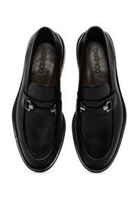 Mocasines de cuero negro con un acabado texturizado, que presentan un detalle de hebilla plateada y un forro interior suave. Diseño de puntera redondeada y suela plana.