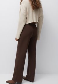 Afgekorte, geribbelde crèmekleurige trui en bruin, high-waisted wijde broek met elastische tailleband, gecombineerd met puntige bruine schoenen.