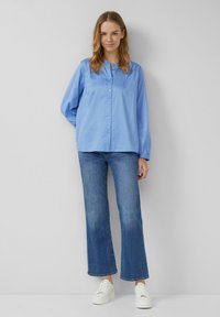 Camicia azzurra chiara con maniche lunghe, caratterizzata da un colletto e una vestibilità rilassata, abbinata a jeans blu a zampa d'elefante e sneakers bianche.
