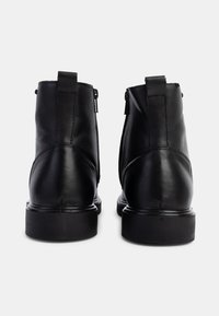 Botas negras de cuero hasta el tobillo con una textura suave, que cuentan con una cremallera lateral y una suela negra resistente. Punta redondeada y detalles de costura mínimos.