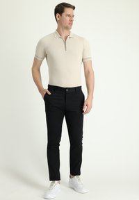Polo de manga corta beige con detalle de cremallera, combinado con pantalones negros ajustados y zapatillas blancas. Tela suave con acentos en contraste.