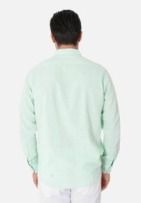 Camicia a maniche lunghe verde menta, tessuto leggero, polsini con bottone, orlo leggermente curvo, dettaglio con spacco sulla schiena. Nessun motivo visibile o decorazioni.