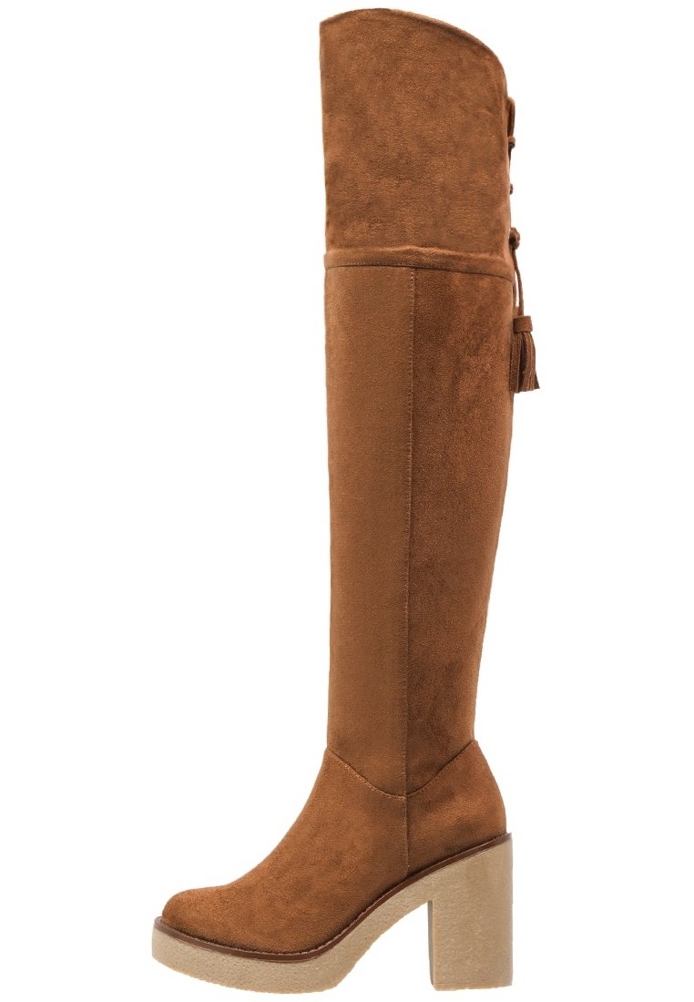Bottes en daim marron au-dessus du genou avec un talon plateforme épais, un bout rond et des franges décoratives à l'arrière. Texture lisse et design ajusté.