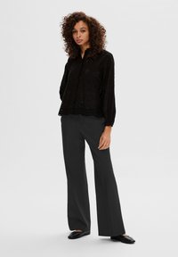 Blusa nera ricamata con orlo scallop, maniche lunghe, chiusura a bottoni e texture a motivo. Abbinata a pantaloni larghi neri.
