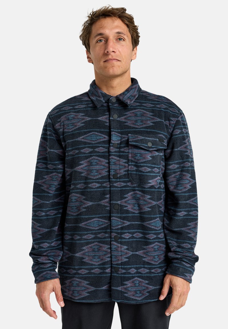 Giacca camicia nera e blu con motivo a diamante, realizzata in tessuto testurizzato. Presenta una chiusura con bottoni e una tasca sul petto.