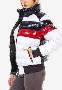 Gepolsterte Steppjacke mit horizontalen Streifen in Marineblau, Rot und Weiß. Hoher Kragen, Reißverschlusstaschen und gerippte Bündchen. Glänzende Oberfläche.