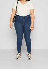 Weißes kurzärmeliges V-Ausschnitt-Shirt, dunkelblaue Skinny-Jeans und grau-rote Sneakers. Einfaches Design mit einer taillierten Silhouette und minimalen Akzenten.