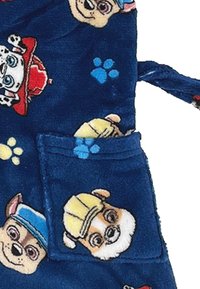 Accappatoio in pile blu con cani dei cartoni animati. Il design include motivi giocosi di facce di cani e impronte di zampe, con una tasca frontale. Texture morbida.