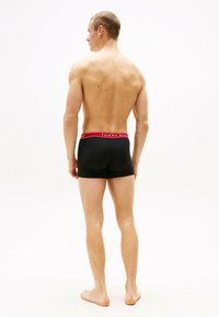 Bóxer negro con cinturilla roja "TOMMY HILFIGER", diseño ajustado, textura suave, mostrando la espalda y la parte superior de las piernas del modelo.