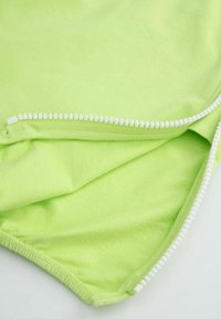 Jasnozielony materiał o gładkiej fakturze z białym suwakiem wzdłuż jednego brzegu. Tkanina wydaje się miękka i lekka.