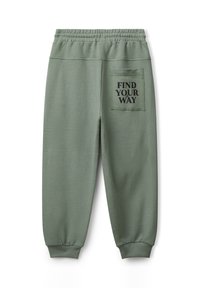 Grüne Jogginghosen mit weichem Material, elastischem Bund und einer Gesäßtasche, die den Text "FIND YOUR WAY" in Schwarz zeigt.