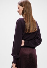 Ljubičasti pleteni pulover s dugim rukavima, rebrastim rubom i opuštenim krojem. Tkanina izgleda mekano s glatkom teksturom i minimalnim detaljima.