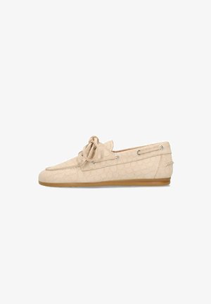 Chaussure style mocassin beige avec motif texturé, lacet noué en nœud sur le dessus et semelle marron, vue de profil gauche.