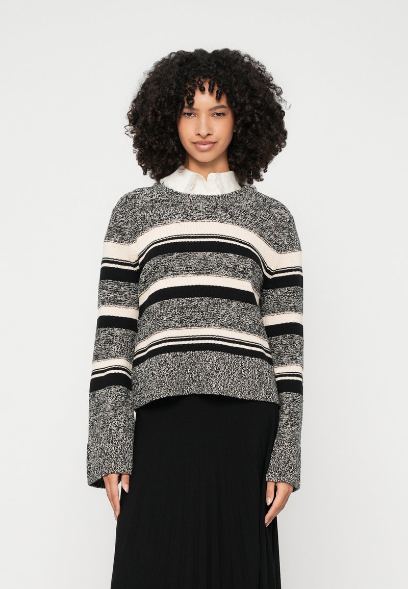 Pleten pulover z oblikovanjem v črno, belo in sivo črtasto zasnovo, kroj prijateljevo ovratnico in širokimi rokavi, v kombinaciji z belo srajco s ovratnikom spodaj.