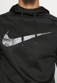 Sudadera negra con cordones ajustables, que presenta un gran logotipo de camuflaje gris de Nike en el frente. Textura de tela suave.