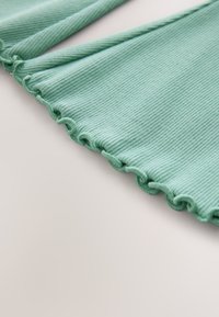 Tela de color verde claro con canaletas y bordes festoneados, tendida sobre una superficie neutra.