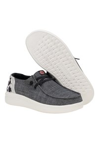 Zapatillas de lona grises con suela blanca, cordones negros y un acento con patrón en el talón. Tejido texturizado con un acabado suave en la suela.