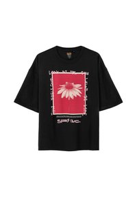 Czarna, oversize koszulka z grafiką przedstawiającą białą stokrotkę na czerwonym tle, otoczoną białym tekstem i różowymi ramkami.