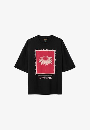 Czarna, oversize koszulka z grafiką przedstawiającą białą stokrotkę na czerwonym tle, otoczoną białym tekstem i różowymi ramkami.