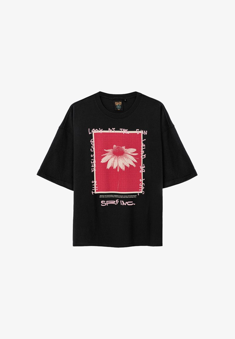 Czarna, oversize koszulka z grafiką przedstawiającą białą stokrotkę na czerwonym tle, otoczoną białym tekstem i różowymi ramkami.