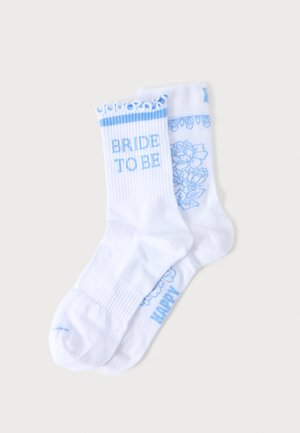 Białe skarpetki z niebieskim tekstem i wzorami, na jednej widnieje "BRIDE TO BE", a druga ma kwiatowe wzory i częściowy tekst.