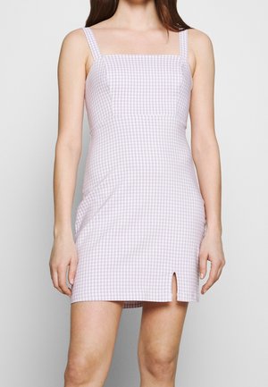 Vrouw draagt een nauwsluitende, mouwloze lila geruite jurk met een vierkante halslijn en een kleine voorsplit bij de zoom.