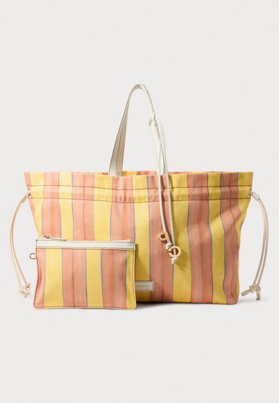 Sac fourre-tout rayé en jaune et rose, avec fermeture à cordon, accompagné d'une petite pochette assortie. Fabriqué en tissu durable, avec des accents blancs.