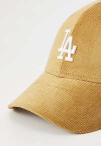 Corduroy cap in mustard yellow with a curved brim. Features a white embroidered 'LA' logo on the front, showcasing a textured finish.
