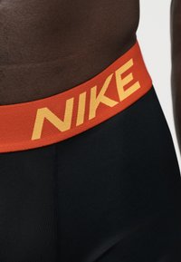 Gros plan d'une personne portant des leggings noirs avec une ceinture orange affichant le logo jaune de Nike.