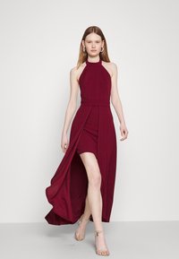 Burgundy halter dress with a fitted bodice and a high slit, showcasing soft fabric and a flowing skirt for a contrasting layered effect.