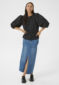 Černý top s nafouknutými rukávy z lehké tkaniny, spárovaný s dlouhou džínsovou sukní s předním rozparkem. Celý outfit doplňují černé robustní boty.