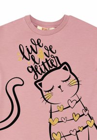 Lys rosa bomulds t-shirt med en sort katte-illustration med glitrende guld accenter, hjerter og teksten "lev elsk glimmer."