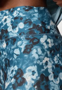 Augstas jostas leggings tumši zaļā audumā ar akvareļu ziedu rakstu melnā un gaiši zilā krāsā. Gluda tekstūra ar redzamām šuvēm.