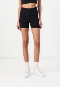 Shorts de sport noirs avec une taille haute et le logo Nike, associés à des baskets blanches et des chaussettes blanches texturées. Tissu lisse et design ajusté.